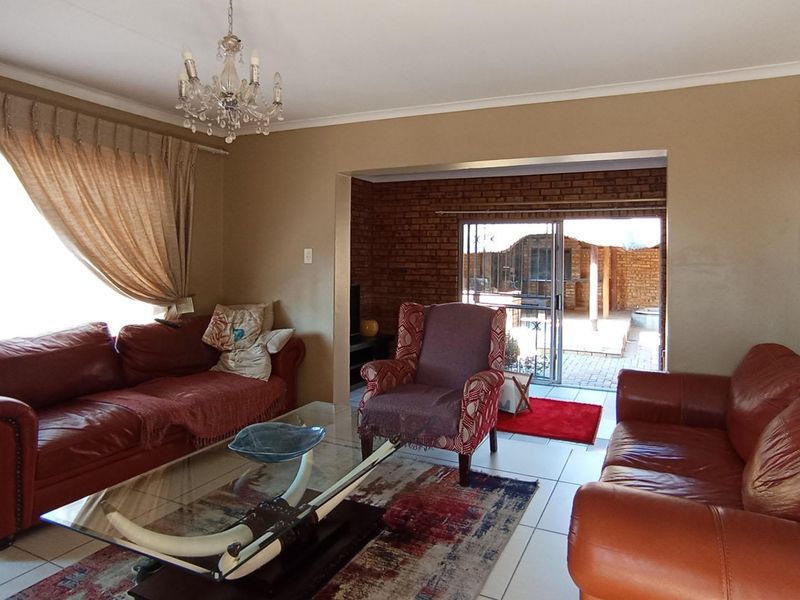 Spacious living room featuring tiled flooring, an exposed brick feature wall, and direct access to an outdoor patio area through sliding glass doors.