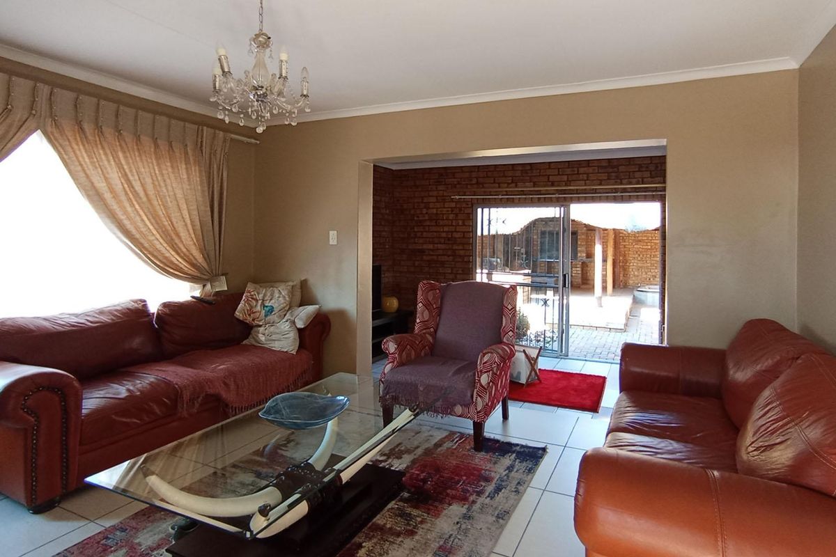 Spacious living room featuring tiled flooring, an exposed brick feature wall, and direct access to an outdoor patio area through sliding glass doors.