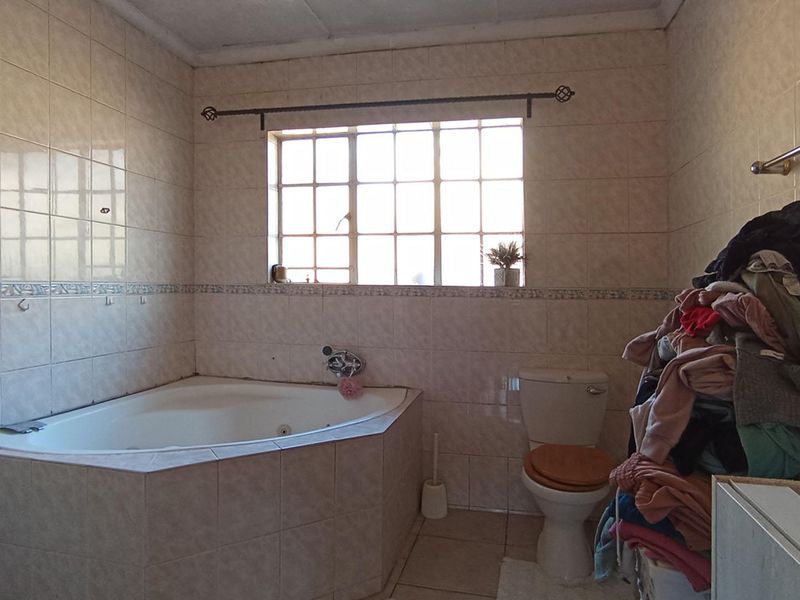 A dated bathroom featuring a built-in corner bathtub, toilet, and full-height wall tiling, requiring modernization to improve its aesthetic appeal.
