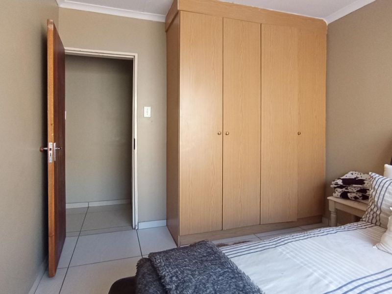A bedroom featuring neutral wall tones, tiled flooring, and a built-in wooden wardrobe, providing functional storage space.