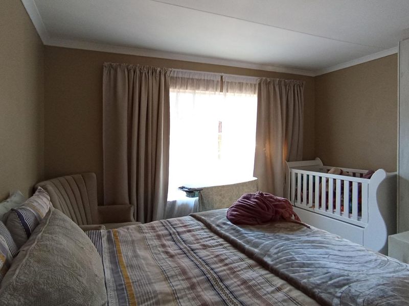 A bedroom featuring neutral wall tones, a built-in wardrobe, and natural light through a window with curtain treatments.