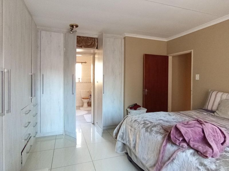 A well-maintained bedroom featuring extensive built-in cupboards, tiled flooring, and direct access to an en-suite bathroom.