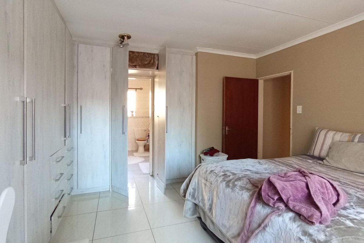 A well-maintained bedroom featuring extensive built-in cupboards, tiled flooring, and direct access to an en-suite bathroom.