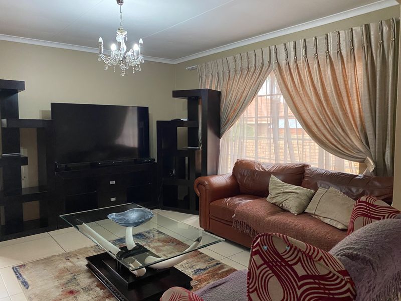 A comfortable living room featuring tiled flooring, ceiling cornice detailing, and large windows with installed curtain tracks.