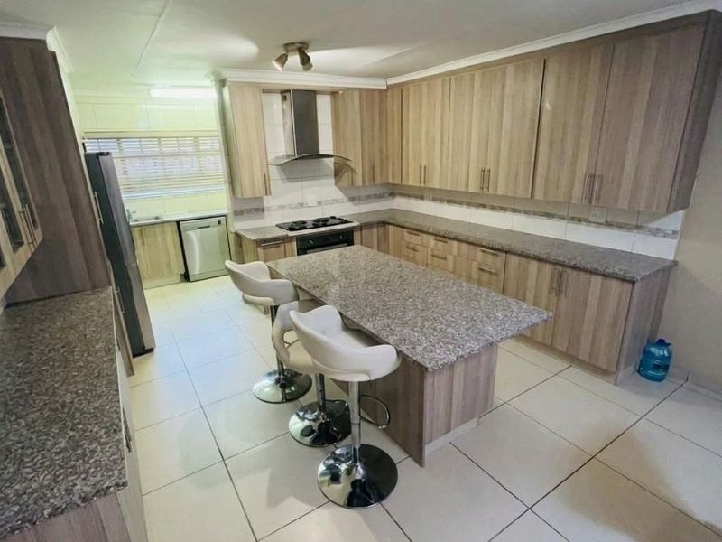 Spacious kitchen featuring wood-finish cabinetry, granite countertops, a central island, and integrated gas hob with extractor fan, complemented by neutral tiled flooring.