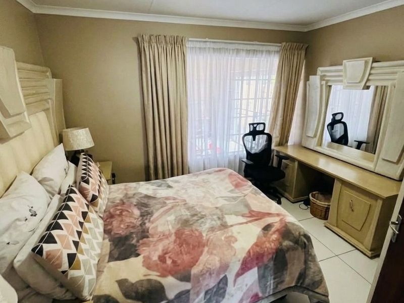 A bedroom featuring tiled flooring, a built-in vanity unit, and large windows with curtain rails, offering a functional and well-lit living space.