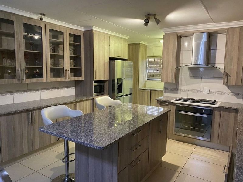 Modern kitchen featuring wood-finish cabinetry, granite countertops, a central island, and integrated stainless steel appliances including an oven, hob, and extractor fan.