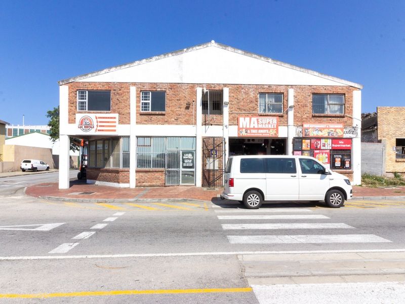 Street-facing view of a two-story industrial building featuring brick construction, multiple storefront entrances, and security gates at street level.
