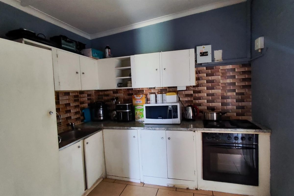 A functional kitchen featuring white cabinetry, tiled backsplash, built-in oven and hob, and tiled flooring, requiring cosmetic updates to modernize the space.