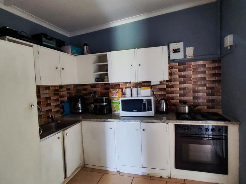 A functional kitchen featuring white cabinetry, tiled backsplash, built-in oven and hob, and tiled flooring, requiring cosmetic updates to modernize the space.
