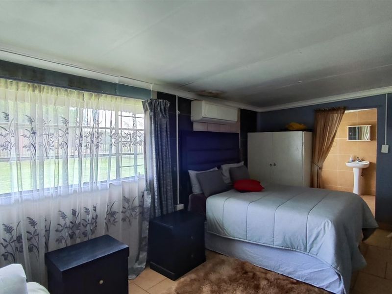 A bedroom featuring tiled flooring, a wall-mounted air conditioning unit, and direct access to an en-suite bathroom.