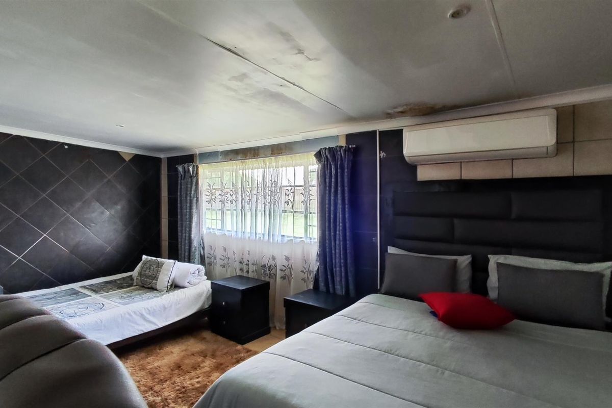 A bedroom featuring a tiled accent wall, split-system air conditioning, and visible ceiling water damage requiring maintenance.