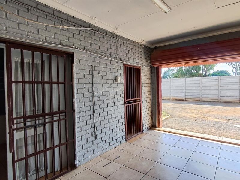 A spacious, empty garage featuring painted brick walls, tiled flooring, and secure metal gates, providing direct access to the exterior driveway.