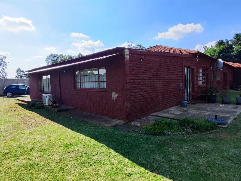 Rear view of a brick farmhouse featuring a concrete patio, tiled roof, and established garden area.