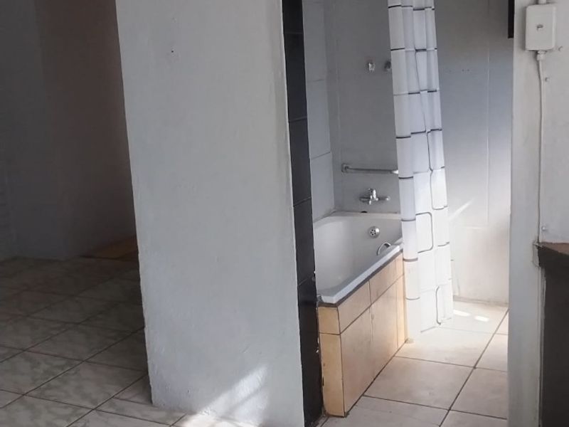 A functional bathroom featuring a built-in bathtub with shower mixer, finished with tiled flooring and neutral wall tones.