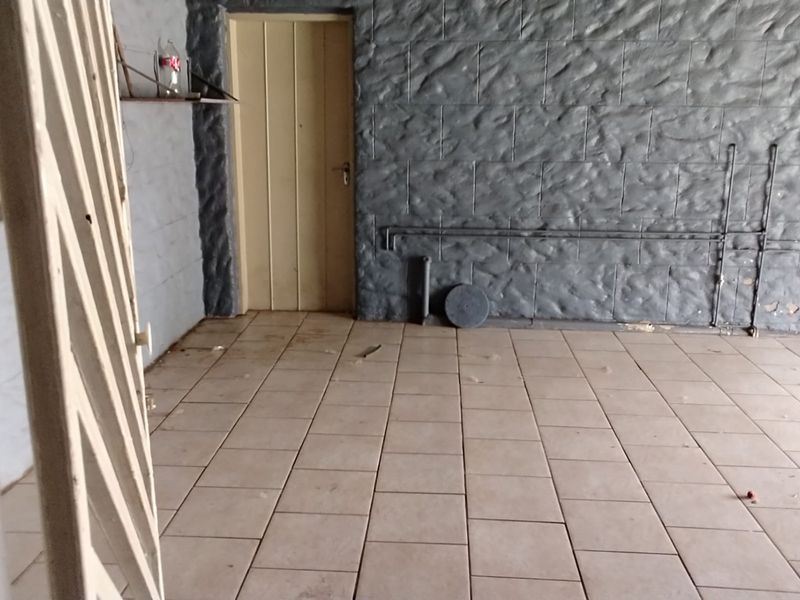 An empty utility space featuring tiled flooring and textured stone-effect wall cladding with exposed surface-mounted piping.
