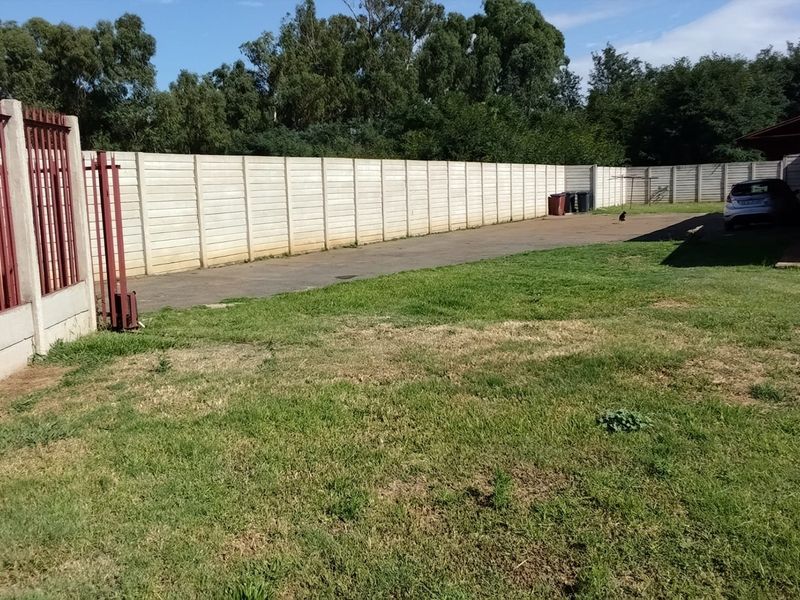 A spacious rear yard featuring a large lawn, paved driveway area, and secure precast concrete boundary walls with metal fencing.