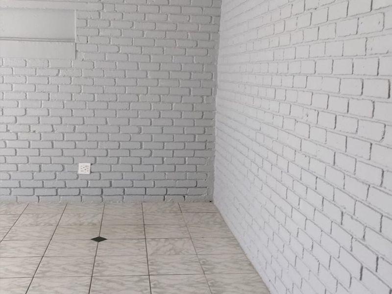 An empty living area featuring painted brick walls, ceramic tiled flooring, and a wall-mounted split-system air conditioning unit.