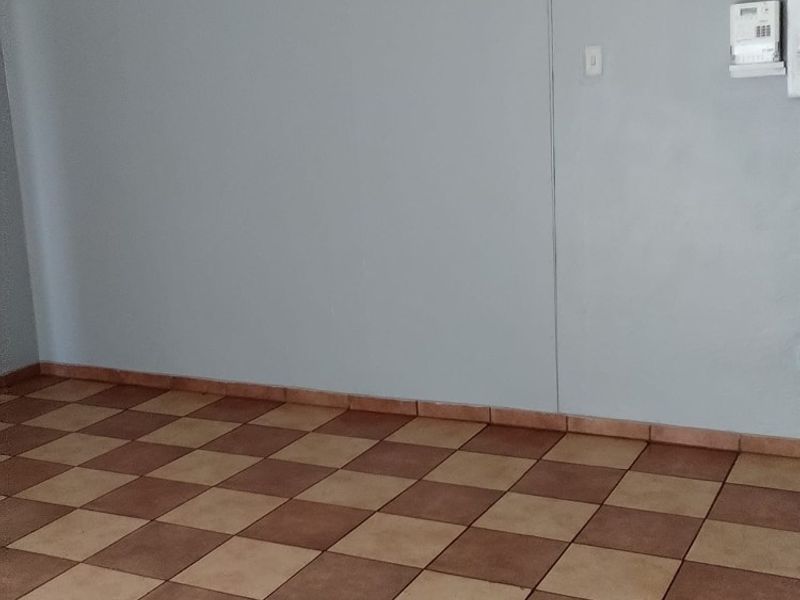 An empty living area featuring neutral painted walls and classic checkered ceramic tile flooring, equipped with a wall-mounted alarm system keypad.