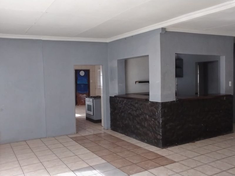 Open plan living area featuring tiled flooring, a stone-clad breakfast bar, and a pass-through window connecting to the kitchen space.