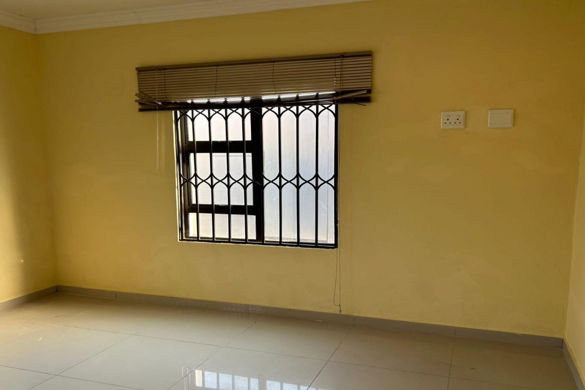 An empty bedroom featuring tiled flooring, yellow walls, and a window fitted with a security gate and blinds.