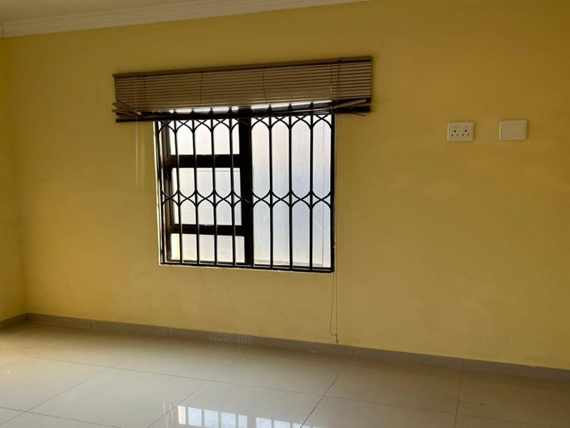 An empty bedroom featuring tiled flooring, yellow walls, and a window fitted with a security gate and blinds.