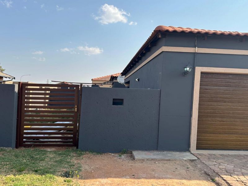 Front exterior view of the property featuring a garage with a roll-up door, a pedestrian gate, and a boundary wall.