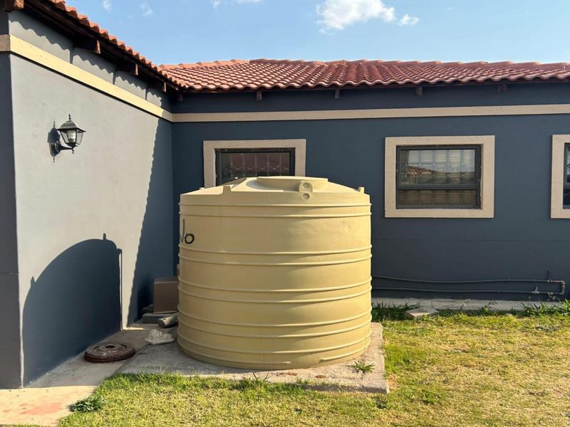 Rear exterior view of the property featuring a large water storage tank on a concrete base, set against a dark-painted wall with tiled roofing.