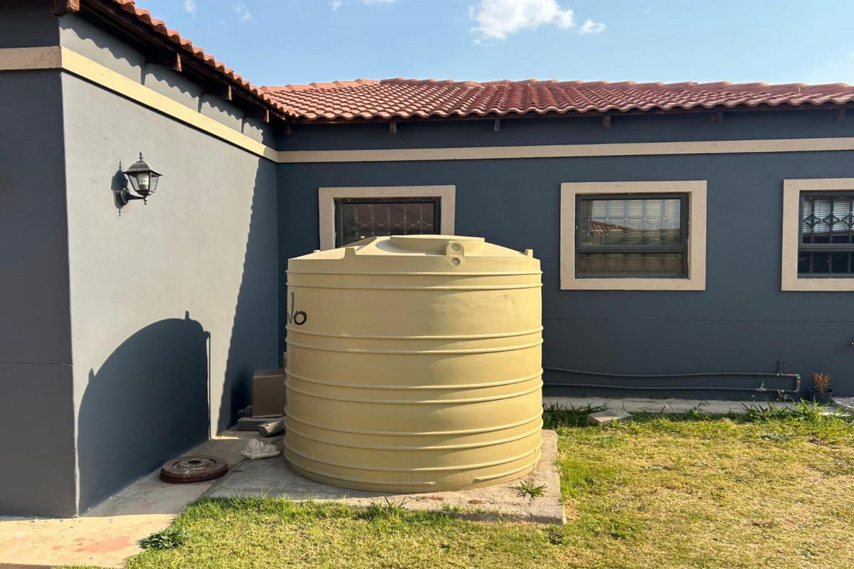 Rear exterior view of the property featuring a large water storage tank on a concrete base, set against a dark-painted wall with tiled roofing.