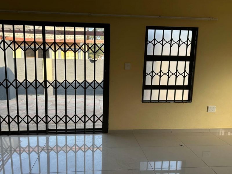 An empty living area featuring tiled flooring, a sliding security gate, and security bars on the window.