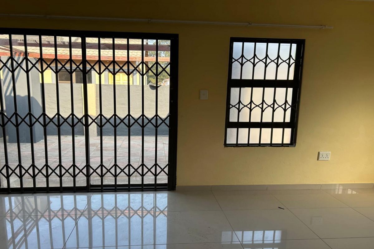 An empty living area featuring tiled flooring, a sliding security gate, and security bars on the window.