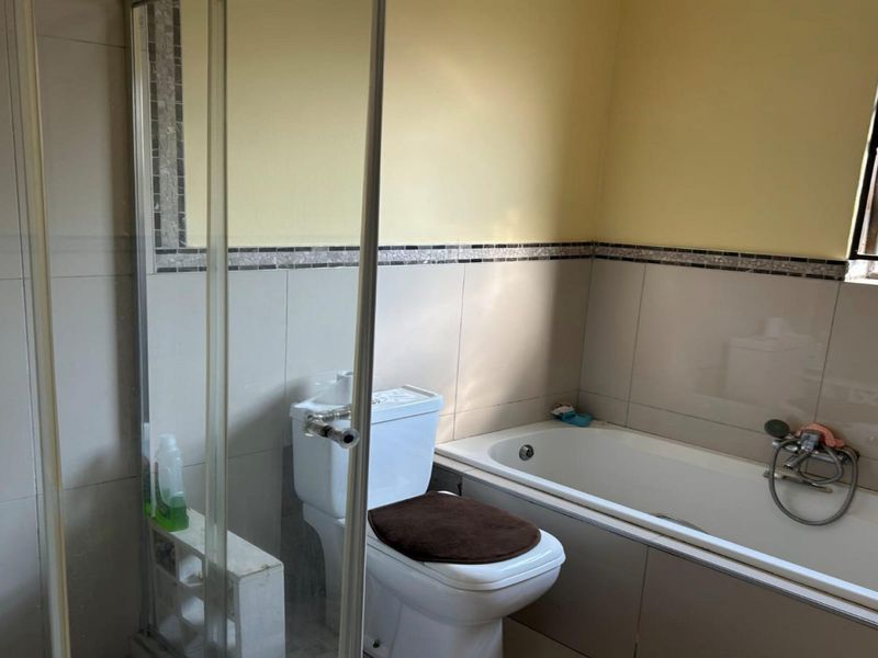 A functional bathroom featuring a shower enclosure, bathtub, and toilet with tiled wall finishes and a window with security bars.
