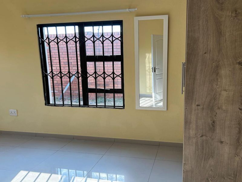 A clean, empty bedroom featuring tiled flooring, a built-in wardrobe, and a window fitted with a security gate.