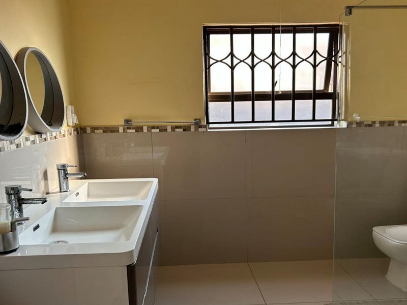 A functional bathroom featuring a double vanity with basin, a toilet, and a glass-enclosed shower area with tiled finishes.