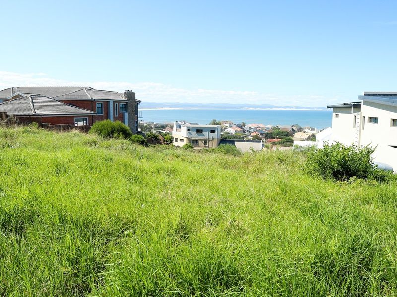 A vacant residential plot featuring a sloped grassy landscape with expansive views of the surrounding coastal neighborhood and ocean.