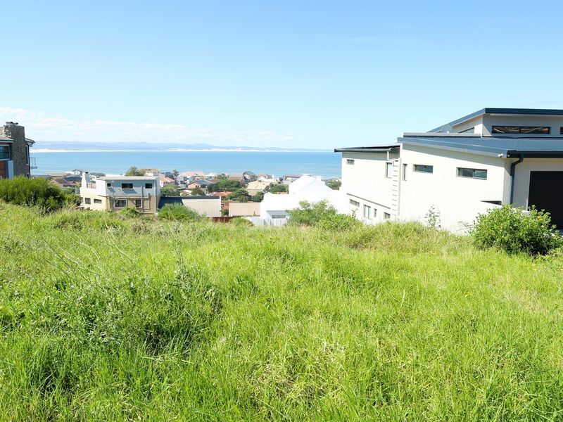 A vacant residential plot featuring a scenic coastal view, situated in a developed neighbourhood with established homes.