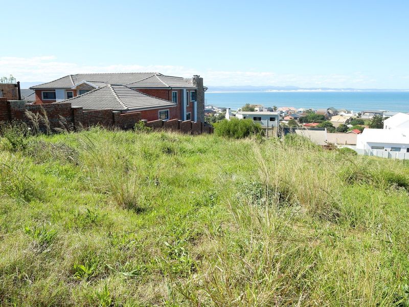 A vacant residential plot featuring a sloped landscape with expansive coastal and ocean views in a developed neighborhood setting.