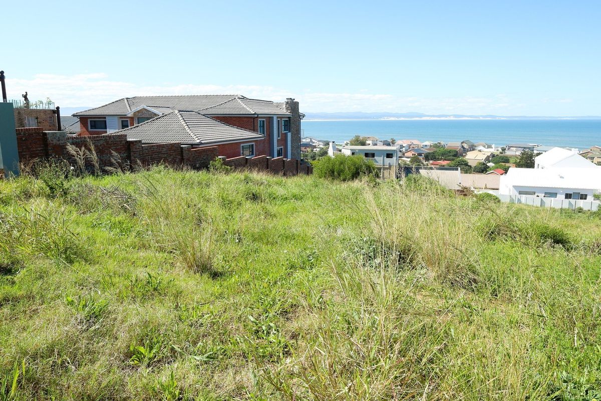 A vacant residential plot featuring a sloped landscape with expansive coastal and ocean views in a developed neighborhood setting.