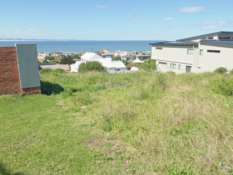 A vacant residential plot featuring a sloped landscape with expansive coastal and neighbourhood views.