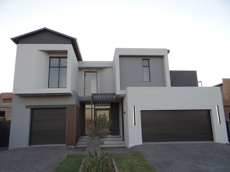 A modern double-story residential facade featuring a combination of grey and white finishes, multiple garage doors, and a paved driveway entrance.