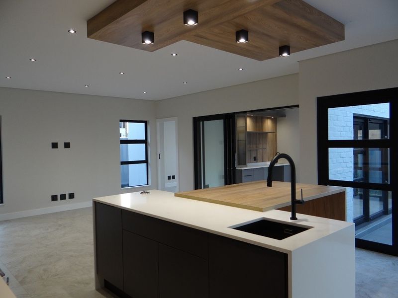 Modern open-plan living area featuring a sleek kitchen island with stone countertops, integrated sink, and stylish timber ceiling detailing with recessed lighting.