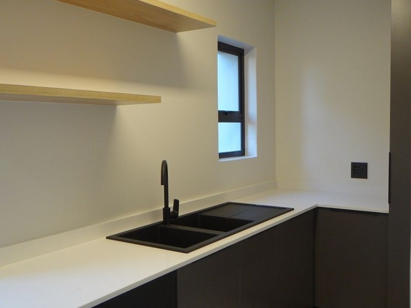 Modern scullery featuring sleek dark cabinetry, white stone countertops, a black double sink, and minimalist floating timber shelving.