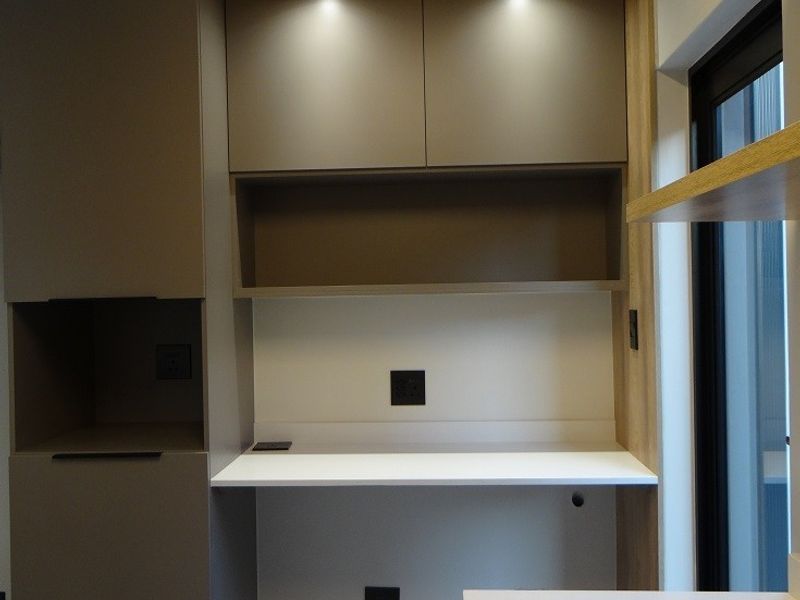 A modern, minimalist built-in home office workspace featuring sleek cabinetry, integrated desk surface, floating shelves, and recessed lighting.