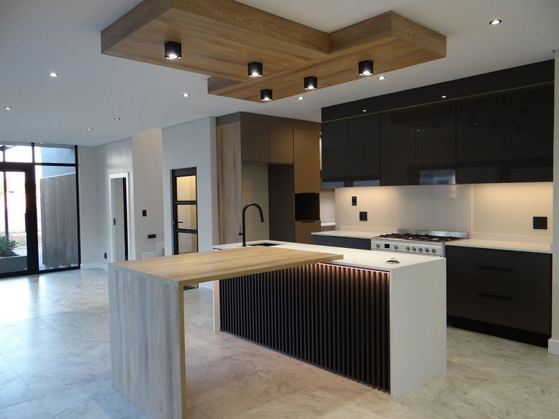 Modern open-plan kitchen featuring a large island with timber breakfast bar, high-gloss cabinetry, gas hob, and integrated lighting in a contemporary neutral space.