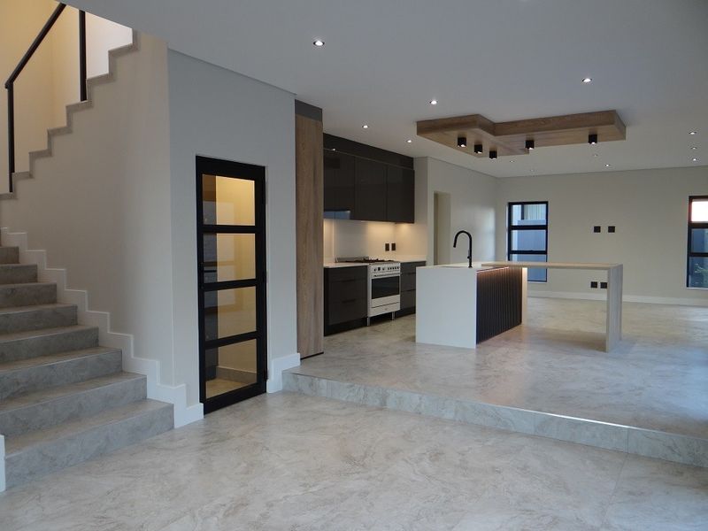 Modern open-plan living area featuring a sleek kitchen with island, integrated lighting, timber ceiling detail, and a contemporary staircase.