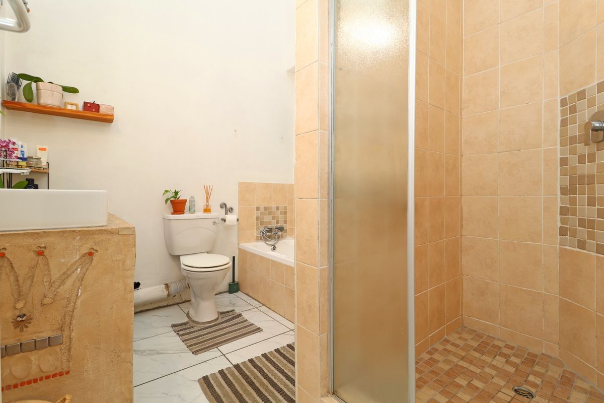 A functional bathroom featuring a separate shower enclosure, bathtub, toilet, and vanity basin with neutral wall and floor tiling.
