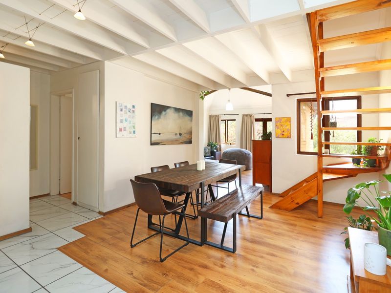 Open-plan living and dining area featuring exposed beam ceilings, a wooden staircase, and a mix of marble-look and laminate wood flooring.