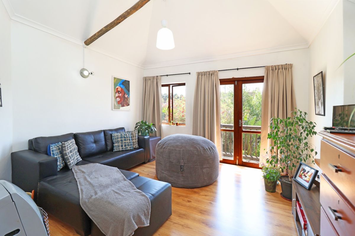 Bright living room featuring a vaulted ceiling with an exposed timber beam, laminate flooring, and direct access to a balcony through timber-framed french doors.