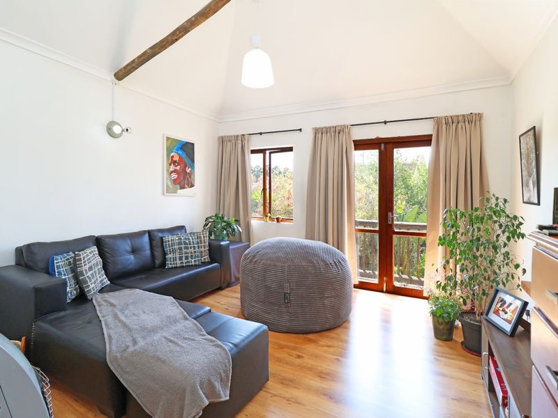 Bright living room featuring a vaulted ceiling with an exposed timber beam, laminate flooring, and direct access to a balcony through timber-framed french doors.