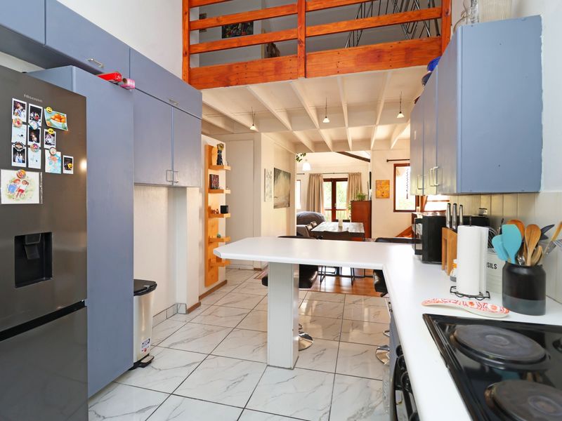 Open-plan kitchen featuring blue cabinetry, a breakfast bar, and tiled flooring, with a view towards the dining area and mezzanine level above.